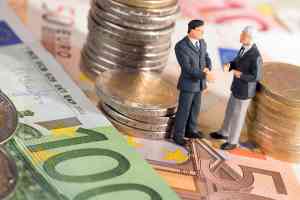 Zwei kleine Figuren stehend auf Geldscheine umringt von Münzen 